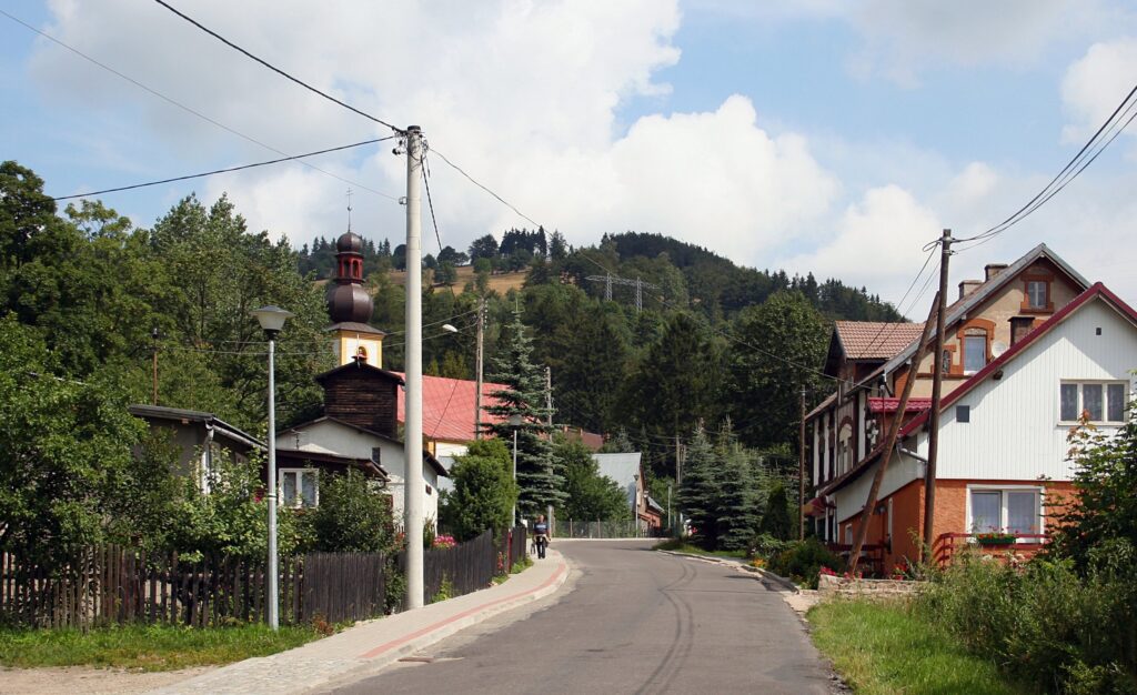 Ulica w Sokolcu z wieżą kościelną i zalesionym zboczem w tle